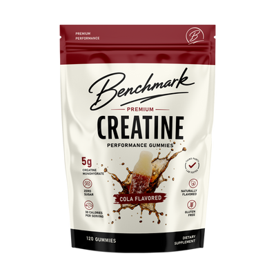 Benchmark Premium Creatine Performance Gummies in a 120-count stand-up pouch, Cola Flavored. The packaging features a white body with a dark red top section and a black bottom band, with a graphic of a cola splash in the center.